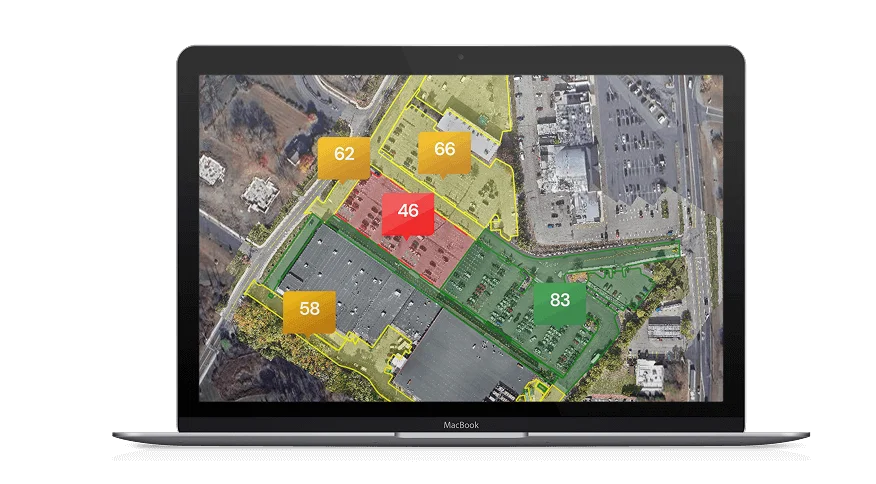 Aerial view of a row of delivery trucks parked at loading bays alongside a large warehouse building. Solar panels cover the buildings roof. Parking spaces are marked by lines on the ground. Adjacent areas have patches of greenery.